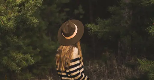 Woman walking through a forest wearing a hat and sweater