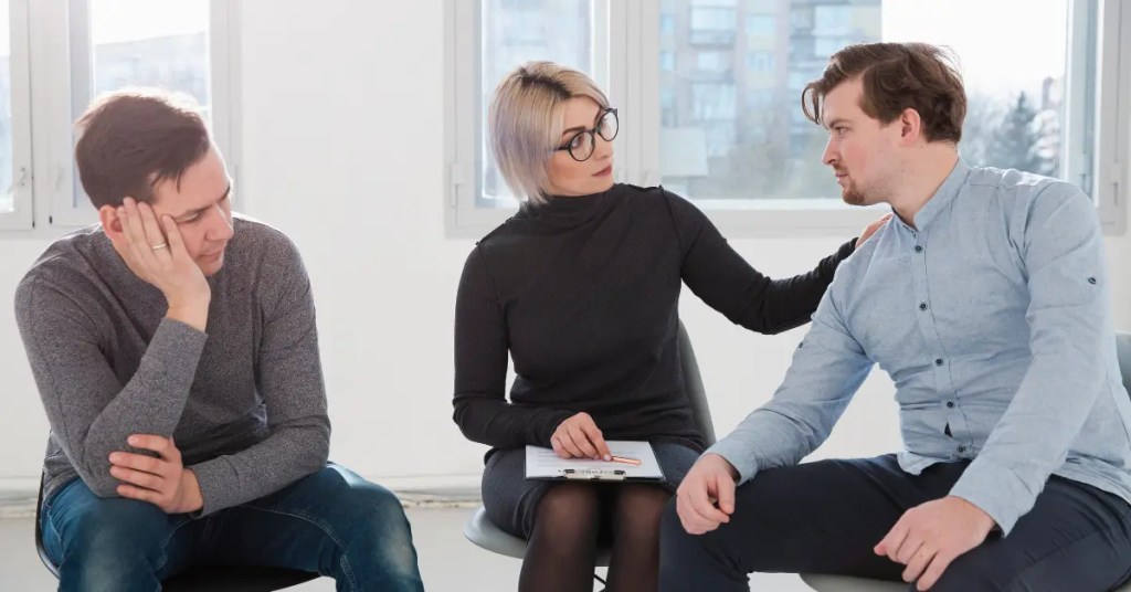 Positive Wellbeing Psychology Melbourne | What Happens to Your Body During a Panic Attack: A Physiological Breakdown Therapist with glasses holding a clipboard and comforting a man while another man sits quietly nearby