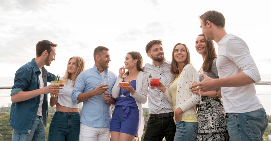 Positive Wellbeing Psychology Melbourne | Social Anxiety vs. Shyness: How to Tell the Difference Group of young adult friends holding cocktails and wine glasses chatting at an outdoor rooftop party