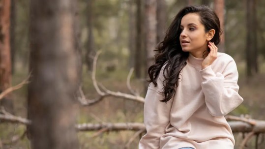 Positive Wellbeing Psychology Melbourne | What Happens to Your Body During a Panic Attack: A Physiological Breakdown Woman with dark wavy hair wearing a cream sweatshirt sitting outdoors in a forest