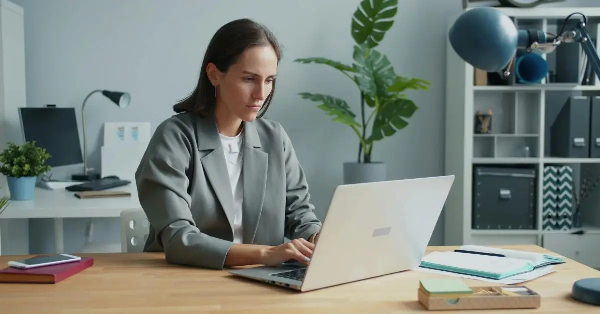 Professional woman sitting at a desk typing on a laptop in a modern office